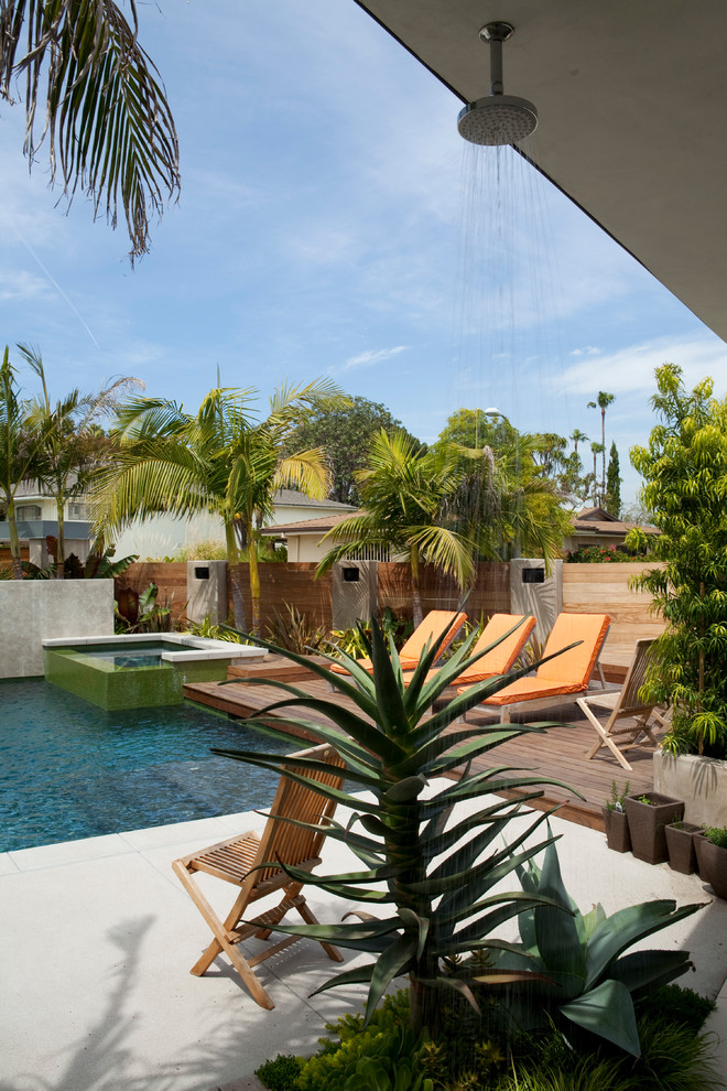 Immagine di una grande piscina tropicale dietro casa con una vasca idromassaggio e lastre di cemento