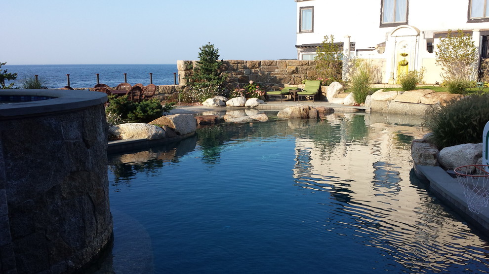 Idée de décoration pour une très grande piscine naturelle et latérale marine sur mesure avec un point d'eau et des pavés en pierre naturelle.