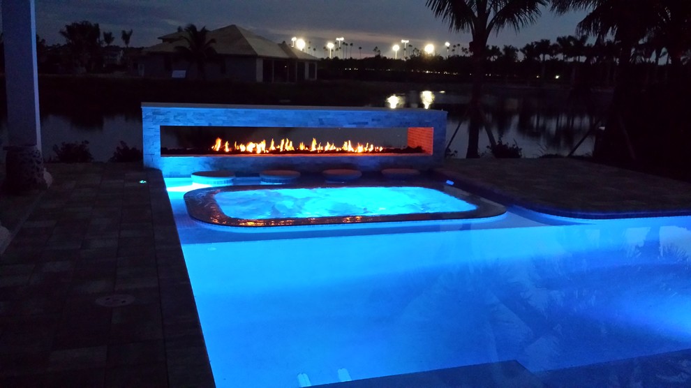Diseño de piscina con fuente alargada mediterránea en forma de L en patio trasero con suelo de baldosas