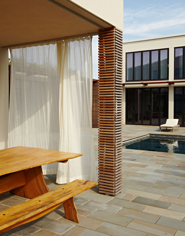Modern back rectangular lengths swimming pool in New York with a pool house and concrete slabs.