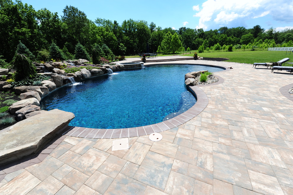 Пример оригинального дизайна: большой спортивный бассейн произвольной формы на заднем дворе в стиле неоклассика (современная классика) с джакузи и покрытием из каменной брусчатки
