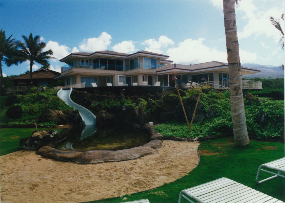 Bild på en mycket stor tropisk rund infinitypool på baksidan av huset, med vattenrutschkana och naturstensplattor