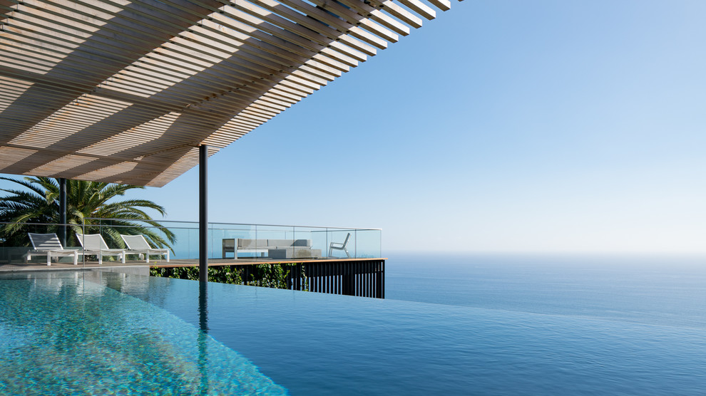 Réalisation d'une grande piscine à débordement et arrière design rectangle avec une terrasse en bois.