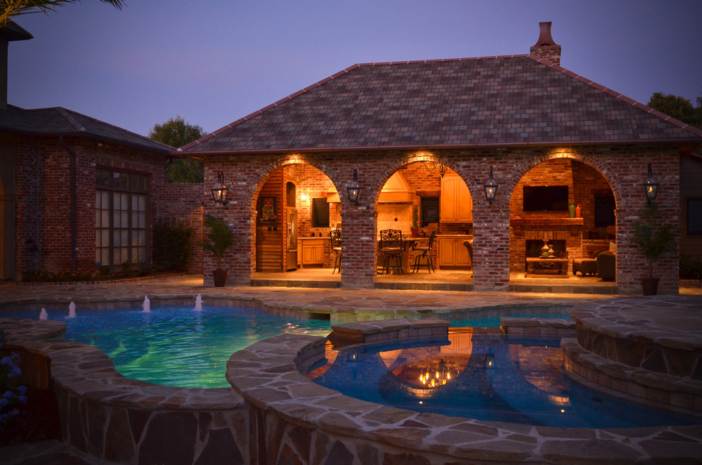 Ejemplo de piscina con fuente tropical grande a medida en patio trasero con adoquines de piedra natural