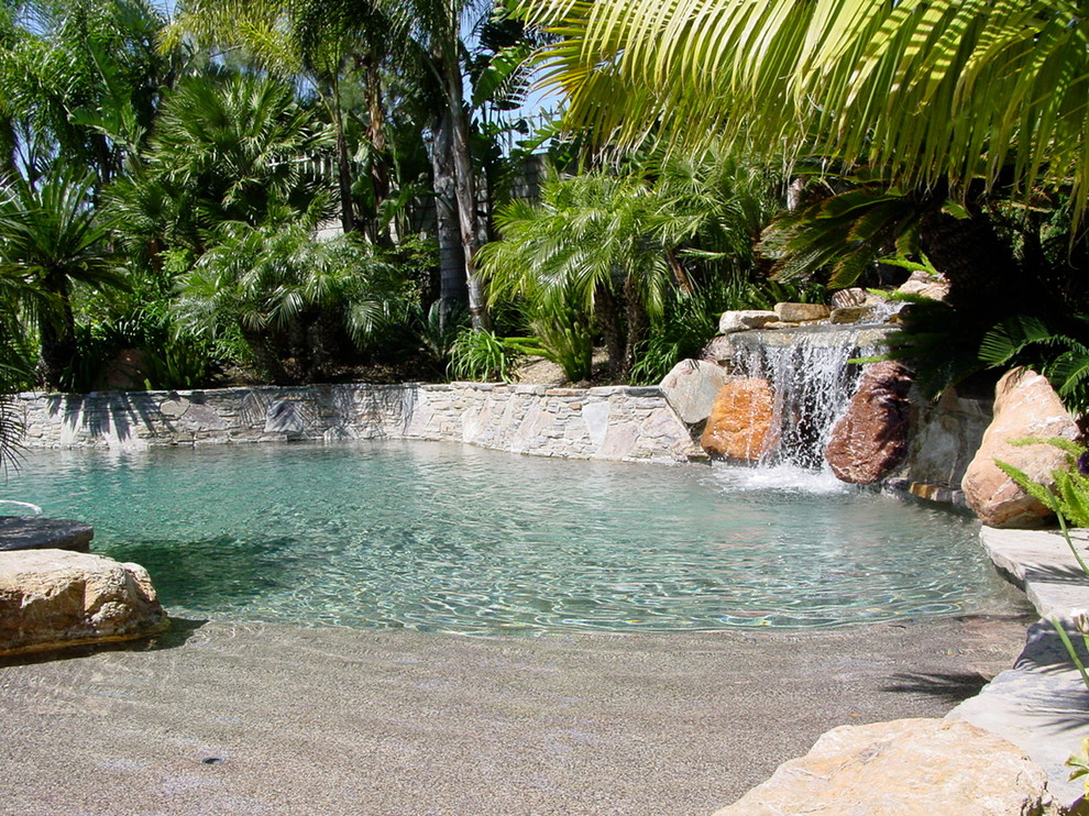 Esempio di una piscina naturale tropicale personalizzata di medie dimensioni e dietro casa con fontane e pavimentazioni in pietra naturale