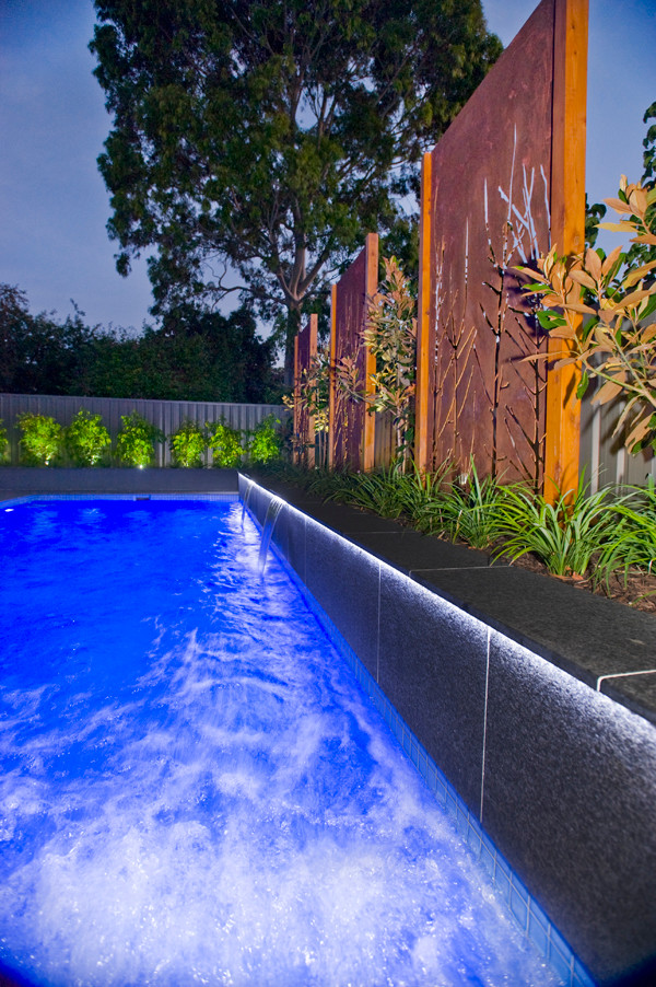 Идея дизайна: прямоугольный бассейн-инфинити среднего размера на заднем дворе в стиле модернизм с покрытием из каменной брусчатки