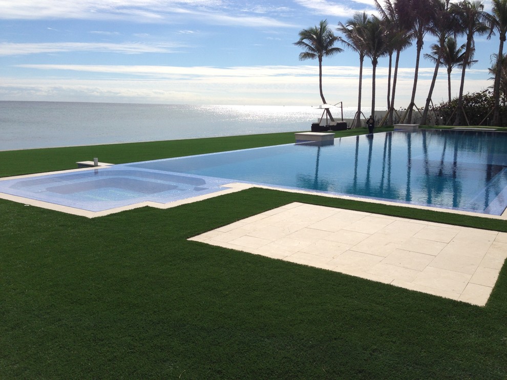 Immagine di una grande piscina a sfioro infinito contemporanea rettangolare dietro casa con lastre di cemento