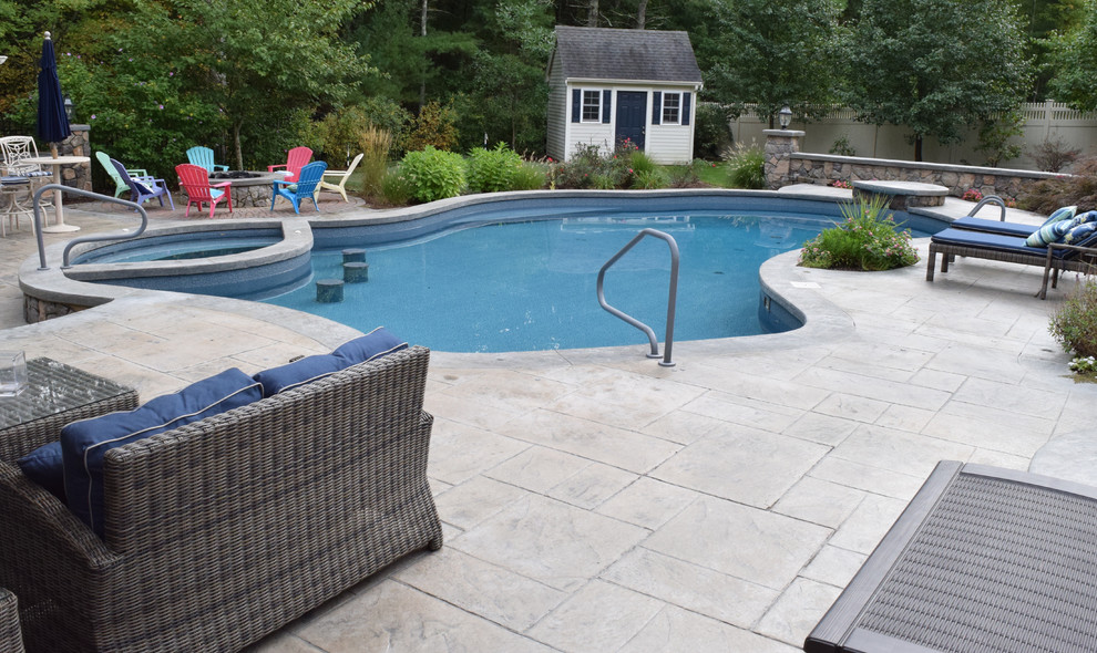 Ejemplo de casa de la piscina y piscina alargada clásica de tamaño medio tipo riñón en patio trasero con suelo de hormigón estampado