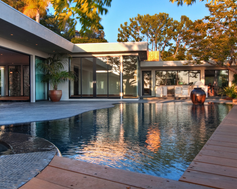 Cette photo montre une grande piscine arrière tendance sur mesure avec un bain bouillonnant et une terrasse en bois.