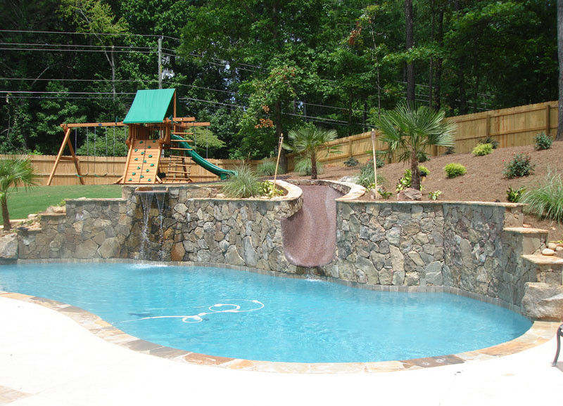 Immagine di una piscina tradizionale personalizzata dietro casa con un acquascivolo e cemento stampato