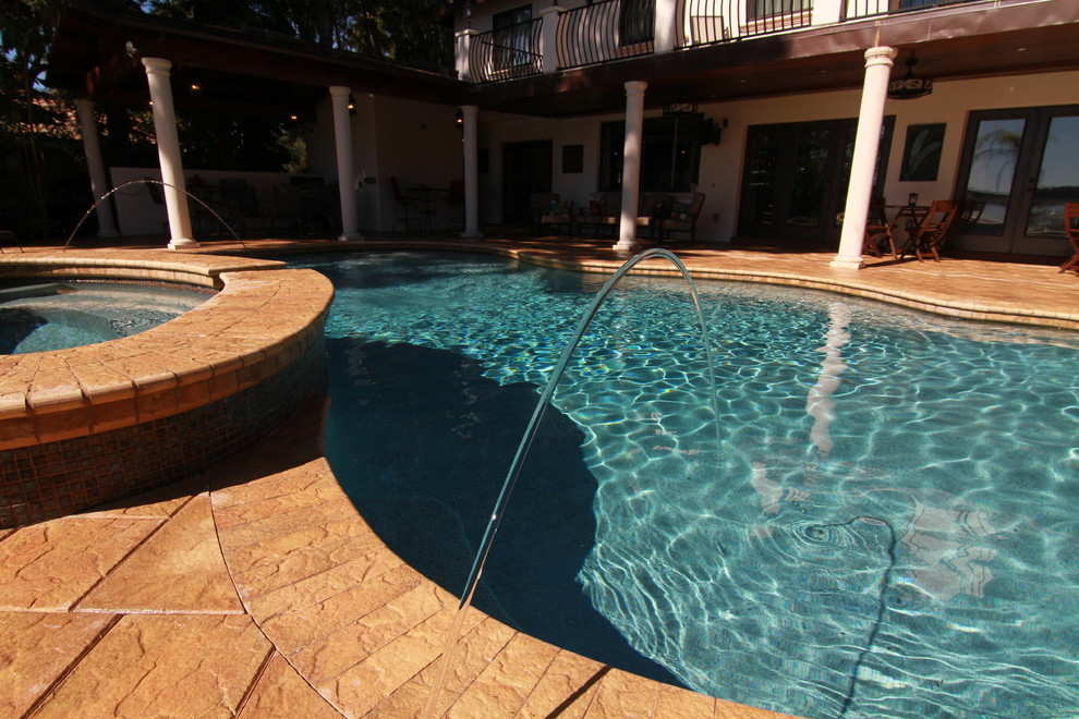Diseño de piscina con fuente natural mediterránea grande en patio trasero con adoquines de hormigón