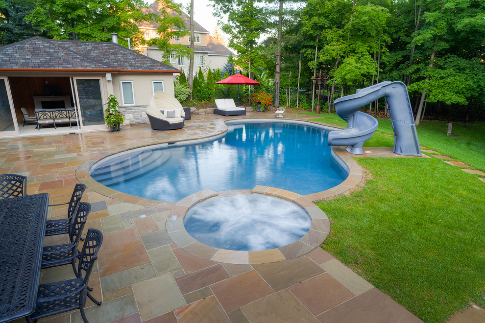 Immagine di una grande piscina tradizionale dietro casa con un acquascivolo e pavimentazioni in pietra naturale