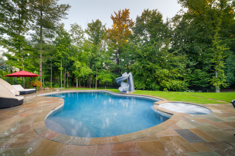 Cette photo montre une grande piscine arrière chic avec un toboggan et des pavés en pierre naturelle.