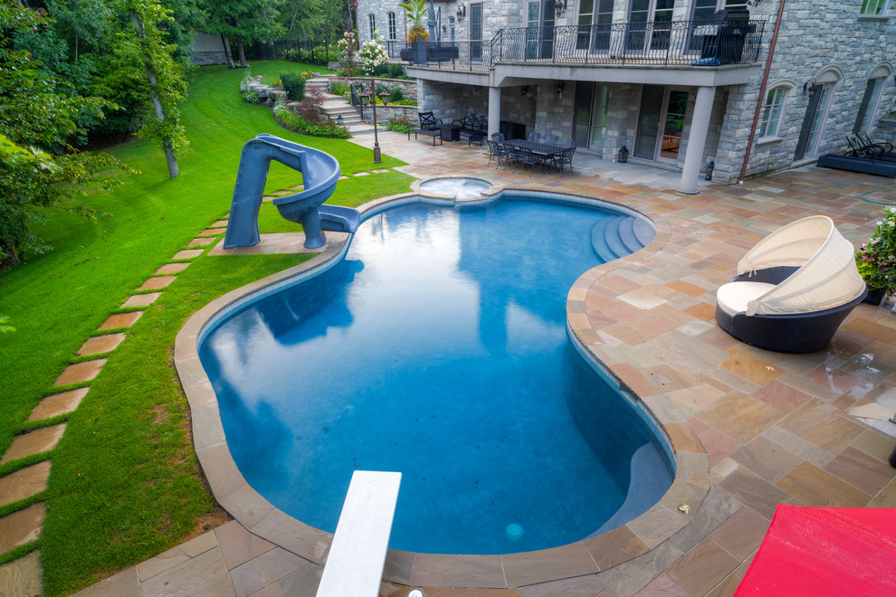 Идея дизайна: большой бассейн произвольной формы на заднем дворе в классическом стиле с водной горкой и покрытием из каменной брусчатки
