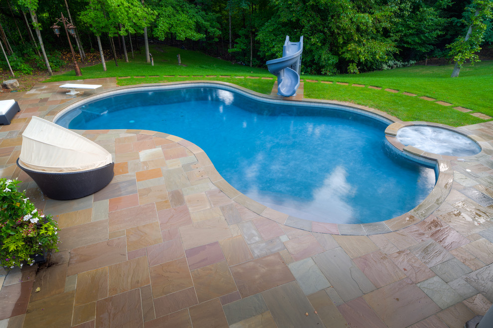 Ejemplo de piscina con tobogán tradicional grande en patio trasero con adoquines de piedra natural