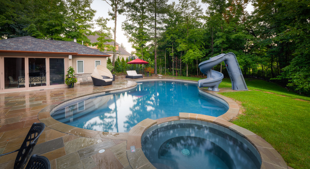 Exempel på en stor klassisk anpassad pool på baksidan av huset, med vattenrutschkana och naturstensplattor