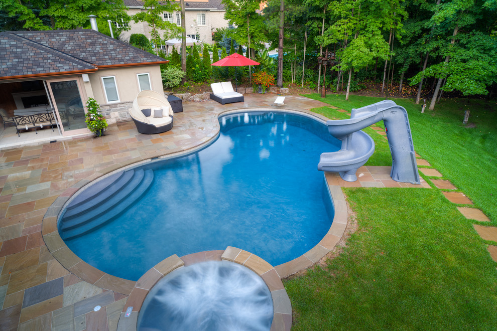Inspiration för en stor vintage pool på baksidan av huset, med vattenrutschkana och naturstensplattor