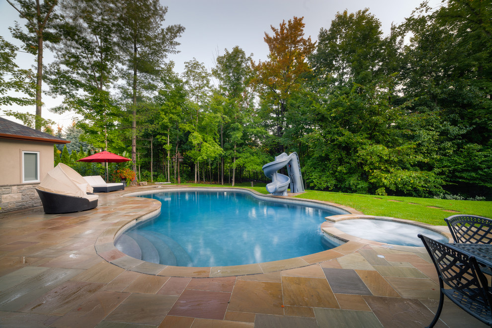 На фото: большой бассейн на заднем дворе в классическом стиле с водной горкой и покрытием из каменной брусчатки