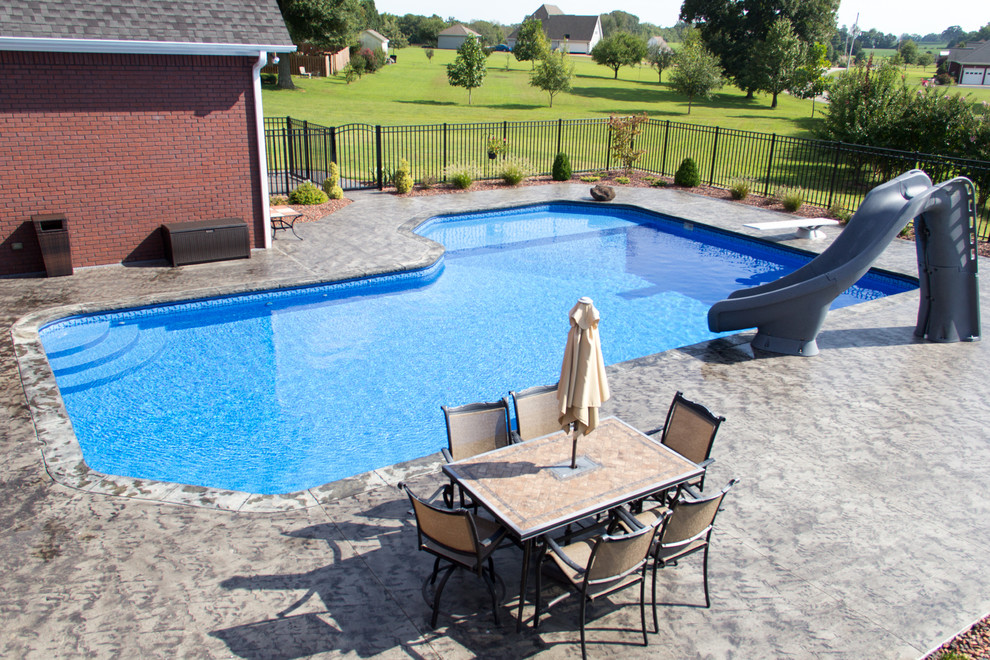 Large classic back custom shaped swimming pool in Chicago with a water slide and concrete slabs.