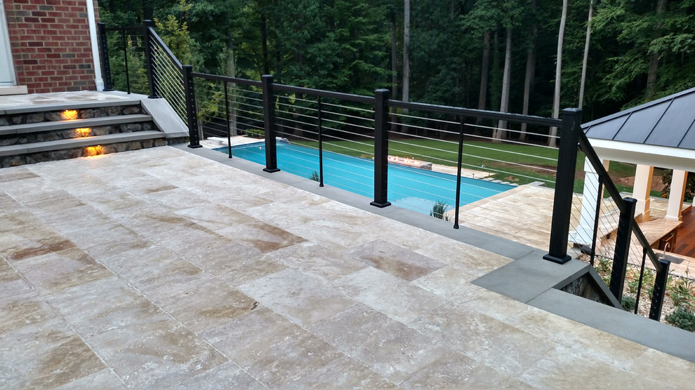 Foto di un'ampia piscina a sfioro infinito minimalista rettangolare dietro casa con una dépendance a bordo piscina e pavimentazioni in pietra naturale