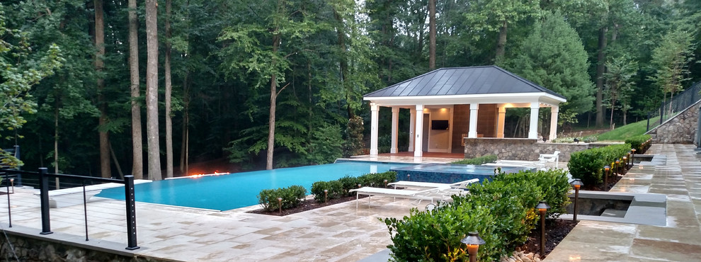 Photo of an expansive modern back rectangular infinity swimming pool in DC Metro with a pool house and natural stone paving.