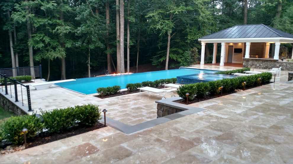 Idee per un'ampia piscina a sfioro infinito moderna rettangolare dietro casa con una dépendance a bordo piscina e pavimentazioni in pietra naturale