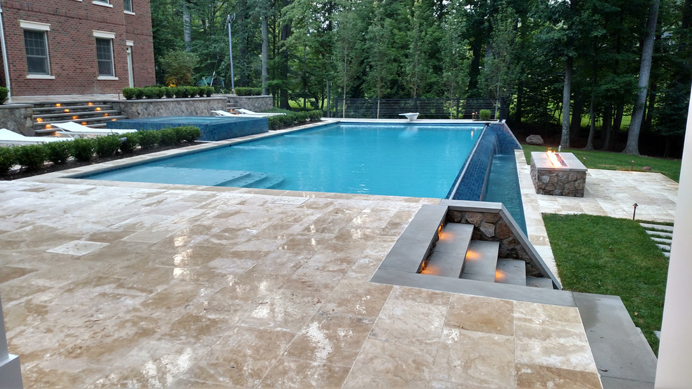 Immagine di un'ampia piscina a sfioro infinito moderna rettangolare dietro casa con una dépendance a bordo piscina e pavimentazioni in pietra naturale