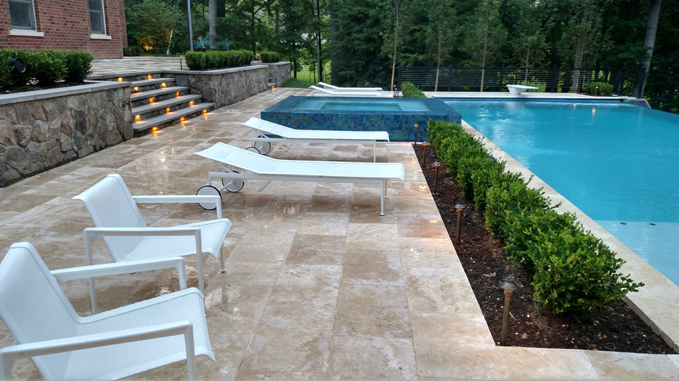 Design ideas for an expansive modern back rectangular infinity swimming pool in DC Metro with a pool house and natural stone paving.