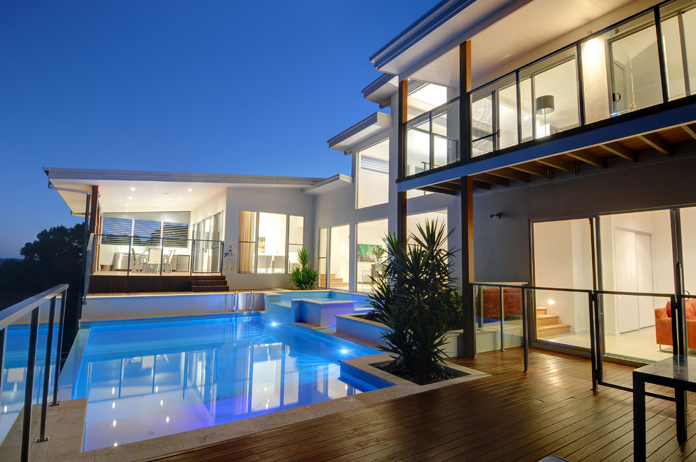 Réalisation d'une grande piscine à débordement minimaliste sur mesure avec une terrasse en bois, une cour et un bain bouillonnant.