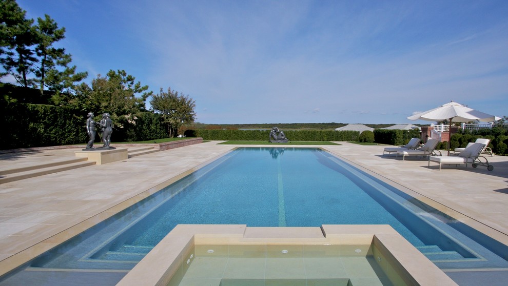 Cette photo montre une grande piscine à débordement et arrière tendance rectangle avec un bain bouillonnant et des pavés en pierre naturelle.