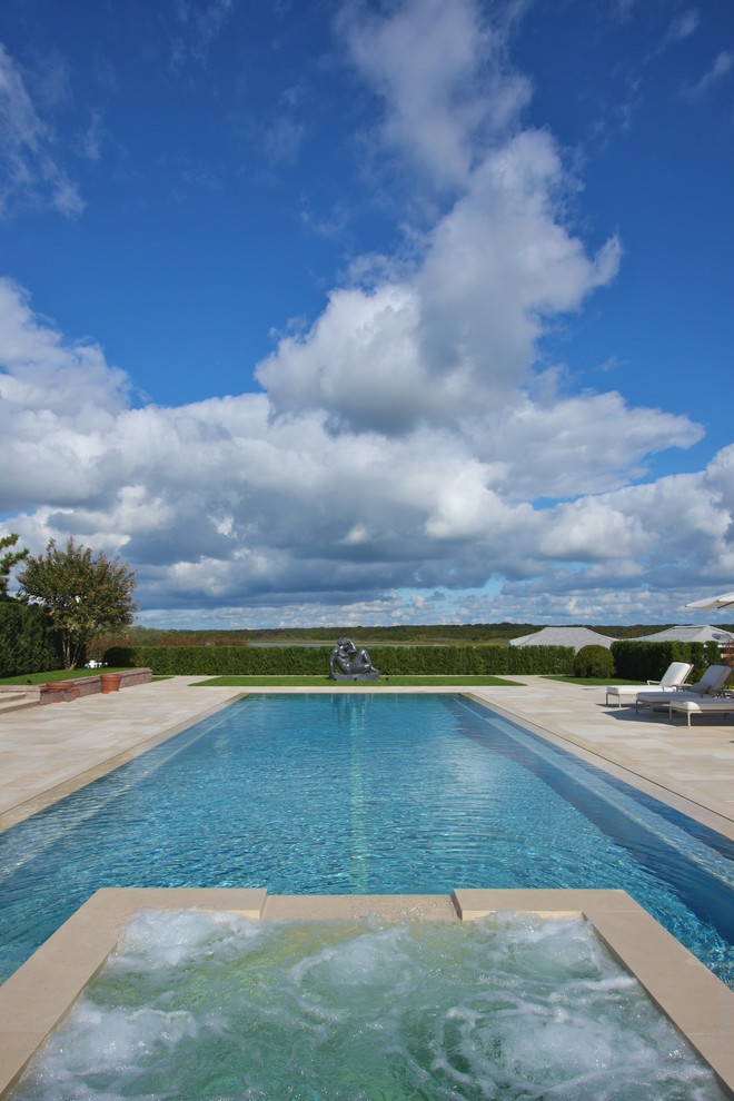 Exemple d'une grande piscine à débordement et arrière tendance rectangle avec des pavés en pierre naturelle et un bain bouillonnant.