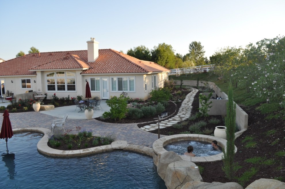 Immagine di una grande piscina naturale mediterranea personalizzata dietro casa con un acquascivolo e pavimentazioni in cemento