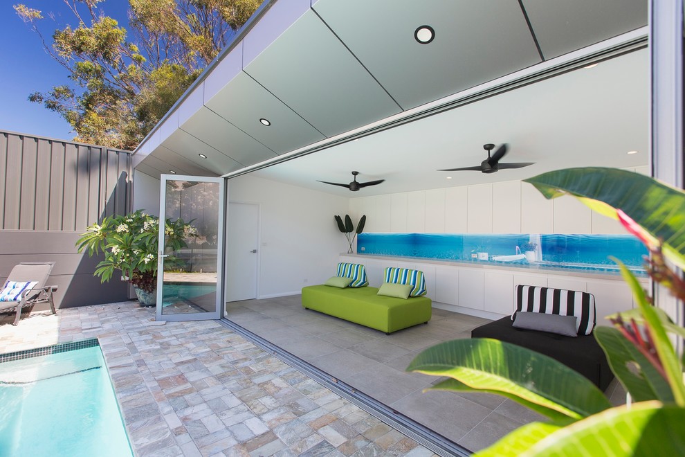 Modelo de casa de la piscina y piscina alargada actual de tamaño medio rectangular en patio trasero con suelo de baldosas