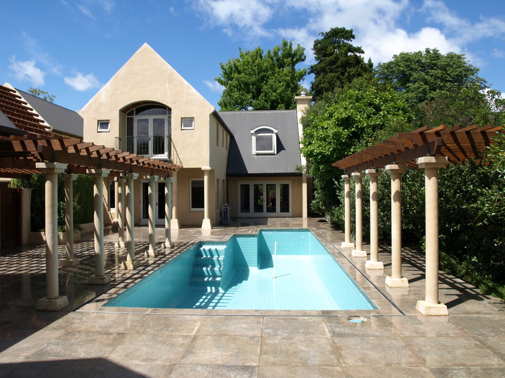 Diseño de piscina actual grande rectangular en patio trasero con suelo de baldosas