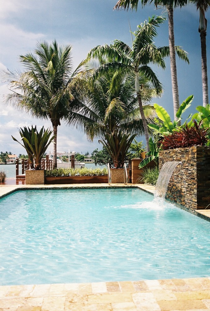 Photo of a large contemporary back rectangular natural swimming pool in Miami with a water feature and concrete paving.