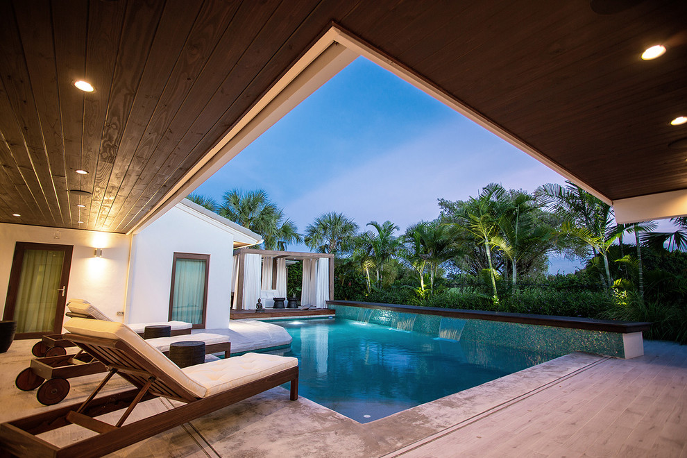 This is an example of a modern back l-shaped natural swimming pool in Miami with a water feature and tiled flooring.