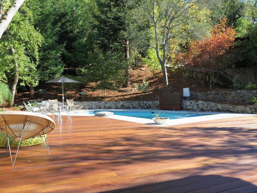 Cette image montre une grande piscine arrière vintage sur mesure avec une terrasse en bois.