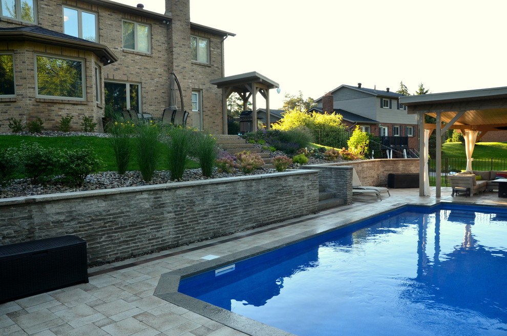 Modelo de piscina actual de tamaño medio rectangular en patio trasero con adoquines de hormigón