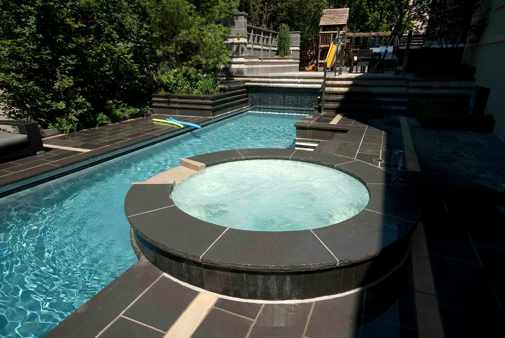 This is an example of a small modern back custom shaped lengths swimming pool in Toronto with a water feature and natural stone paving.