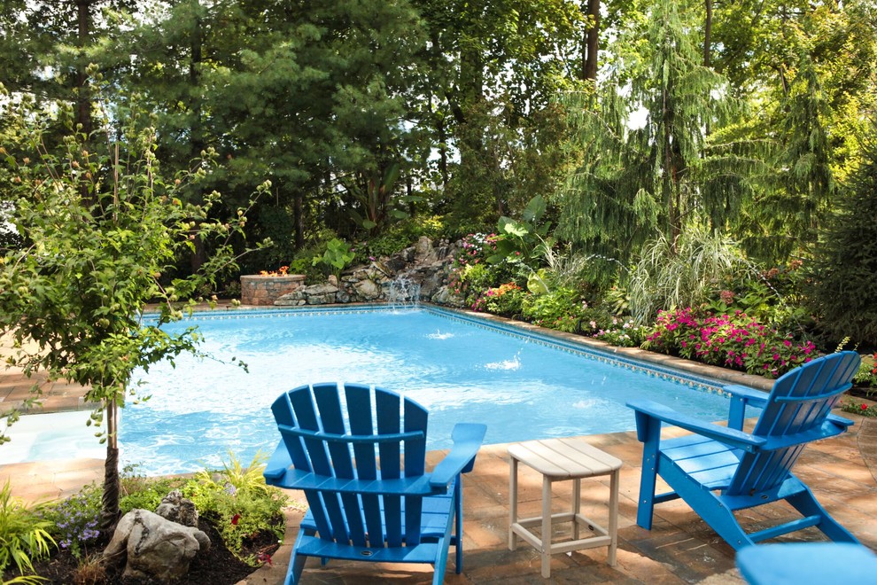 Immagine di una grande piscina monocorsia tropicale rettangolare dietro casa con fontane e piastrelle