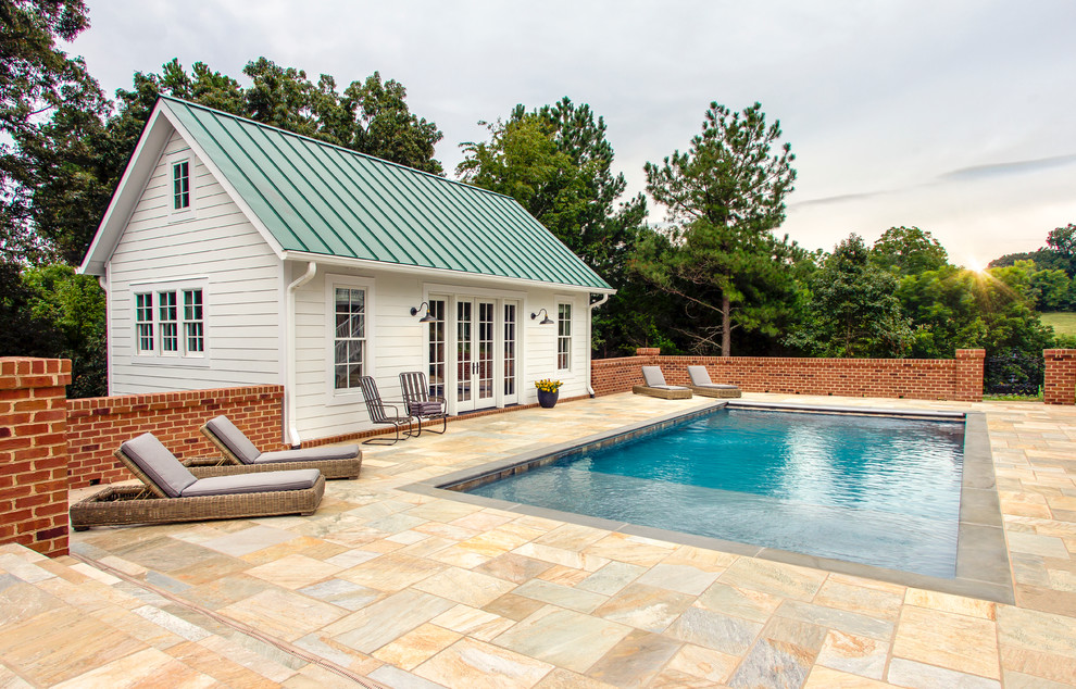 This is an example of a large rural back rectangular swimming pool in Other with a pool house and natural stone paving.