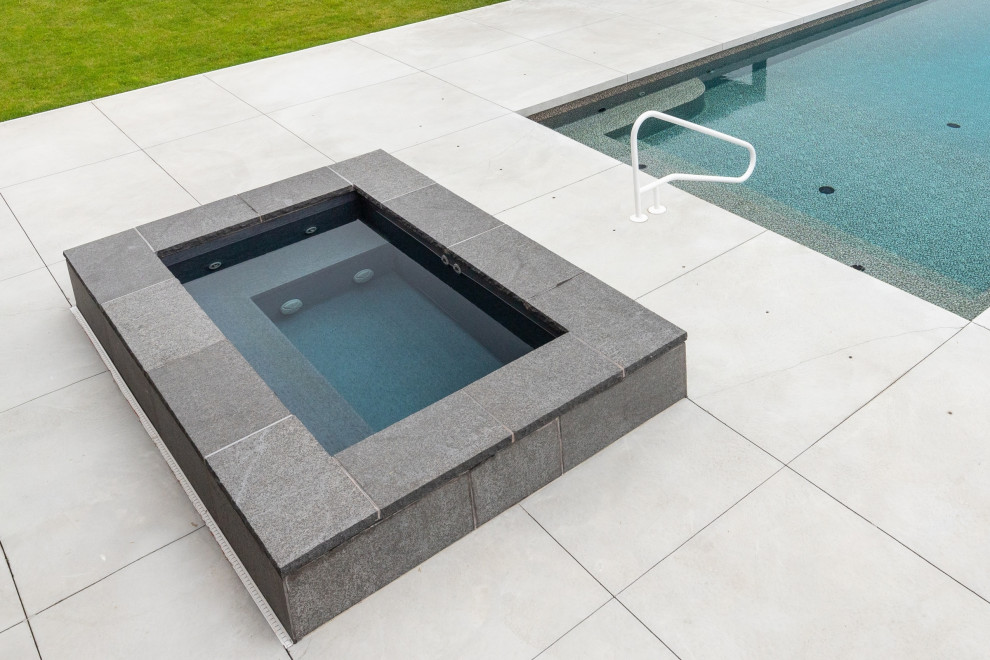 Immagine di una piscina contemporanea rettangolare di medie dimensioni e dietro casa con una vasca idromassaggio e lastre di cemento