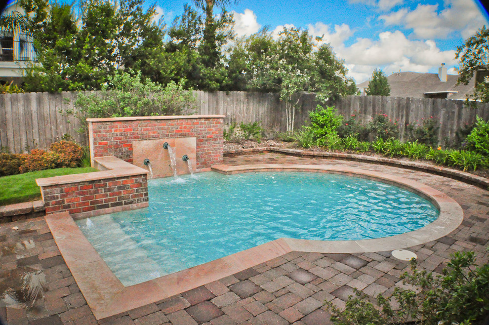 Ejemplo de piscina tradicional pequeña redondeada en patio trasero con adoquines de piedra natural