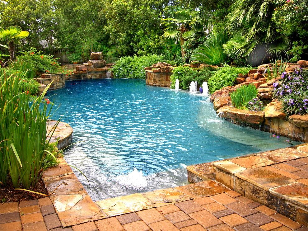 Réalisation d'une grande piscine arrière tradition sur mesure avec un point d'eau et des pavés en pierre naturelle.