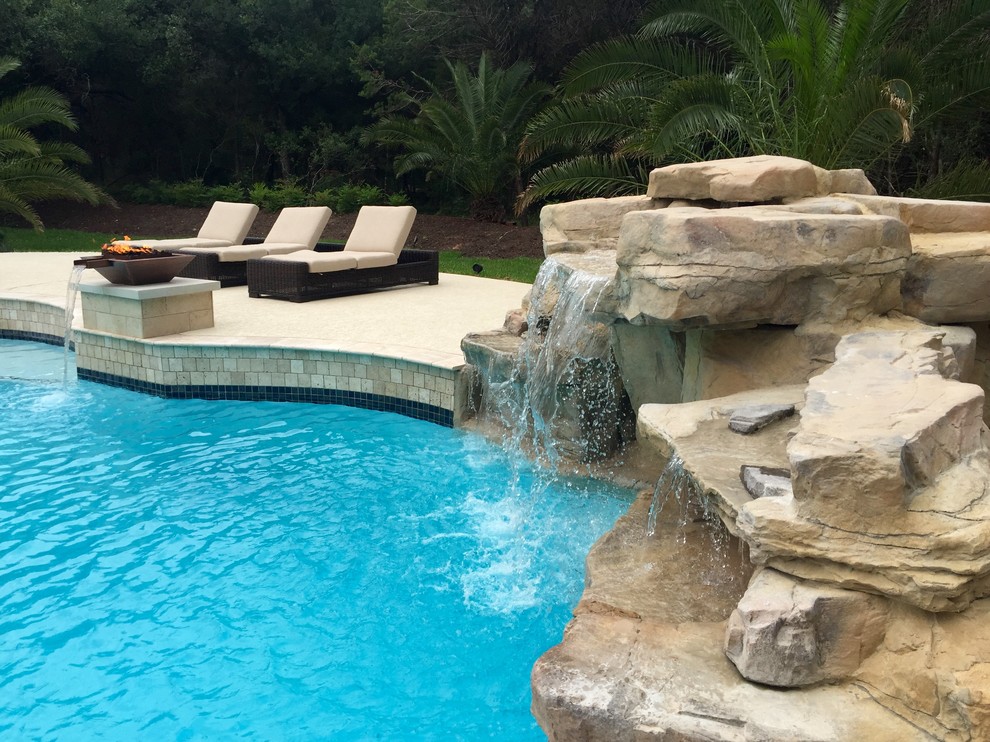 Idée de décoration pour une grande piscine naturelle et arrière design en forme de haricot avec un point d'eau et des pavés en pierre naturelle.