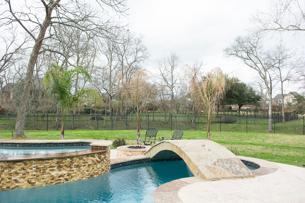 Cette photo montre une grande piscine arrière chic sur mesure avec un bain bouillonnant et des pavés en pierre naturelle.