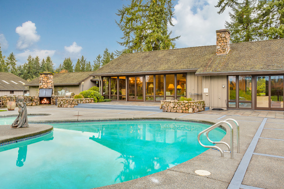 Large country backyard concrete paver and custom-shaped lap pool photo in Seattle