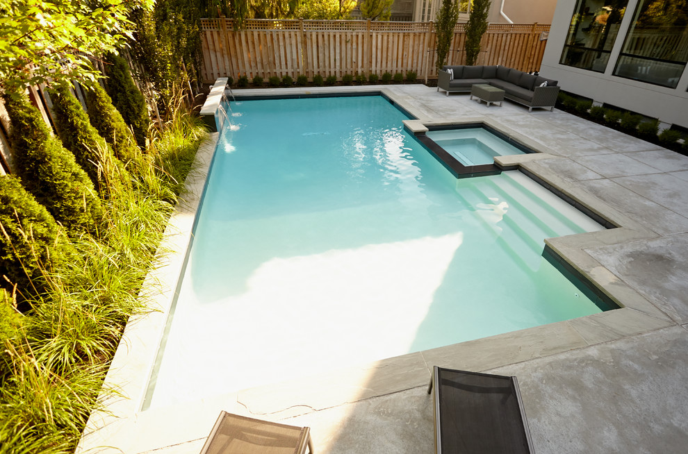 На фото: большой бассейн произвольной формы на заднем дворе в стиле модернизм с джакузи и покрытием из бетонных плит с