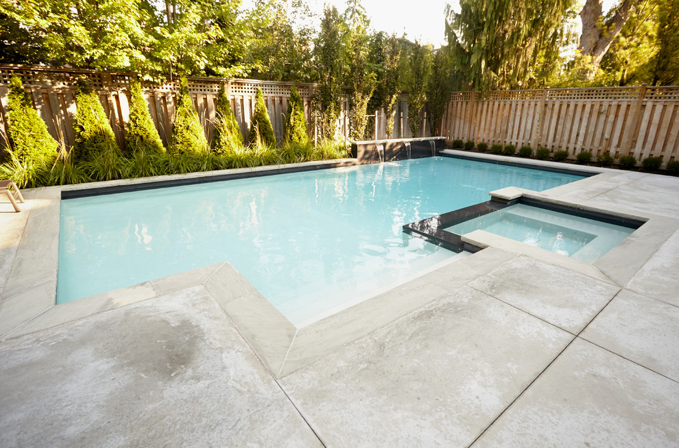 Immagine di una grande piscina minimalista personalizzata dietro casa con una vasca idromassaggio e lastre di cemento