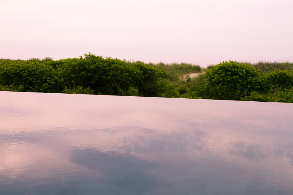 Cette image montre une grande piscine à débordement et arrière minimaliste rectangle avec une terrasse en bois.